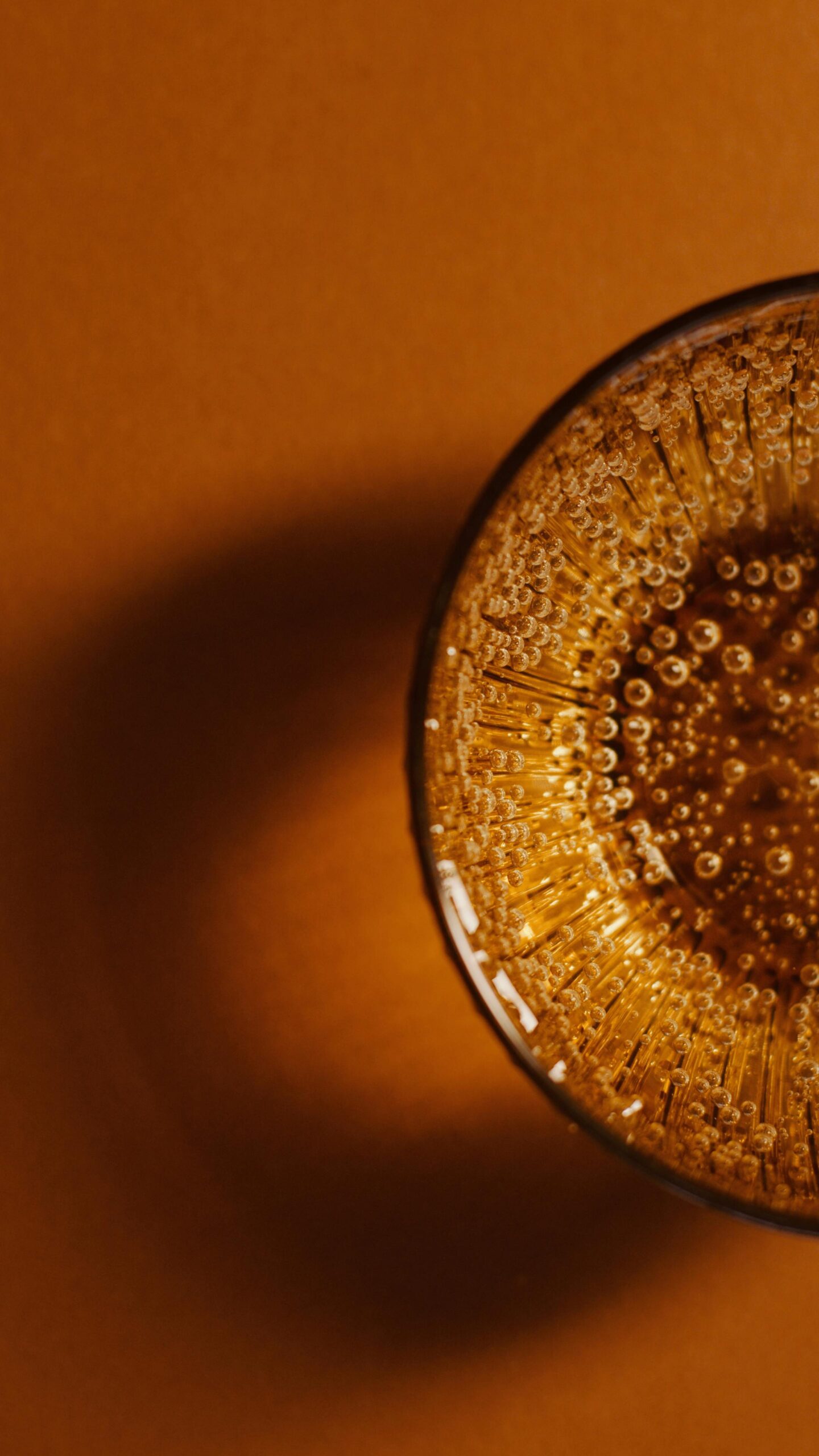 Overhead shot of a fizzy drink with bubbles in a glass on a brown surface.