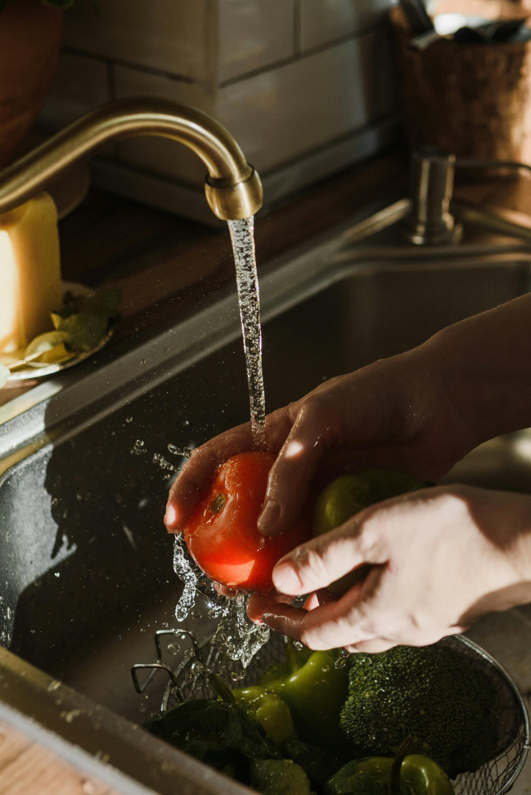Close-up of hands washing a ripe tomato under a kitchen faucet. Perfect for themes of cleanliness and healthy living.
