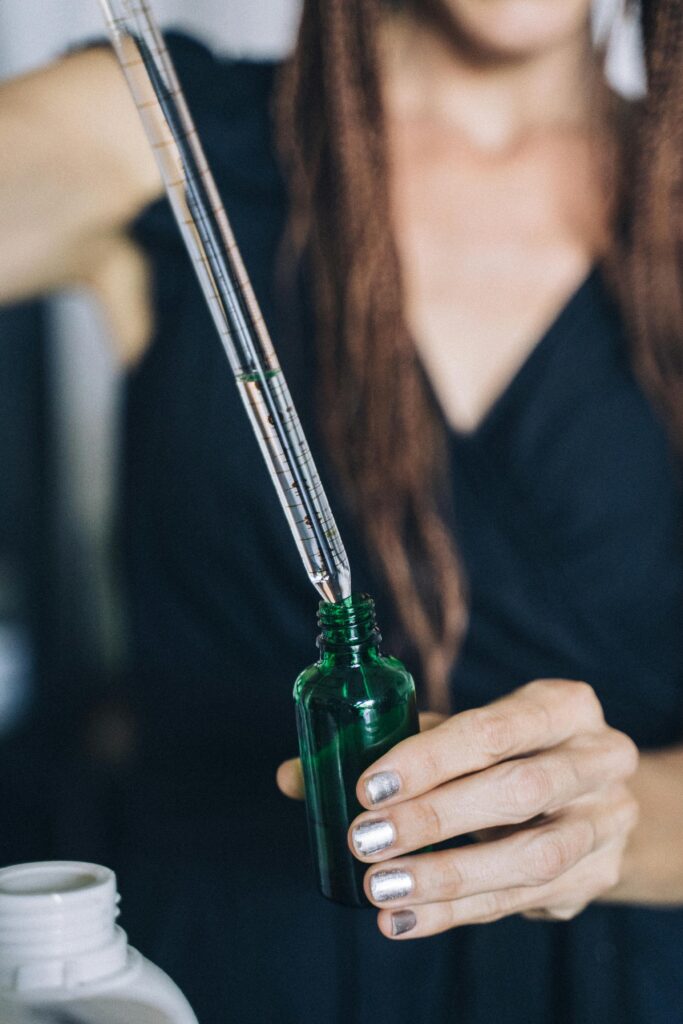 Close-up of hands refilling a reusable glass bottle using a dropper, emphasizing sustainability.